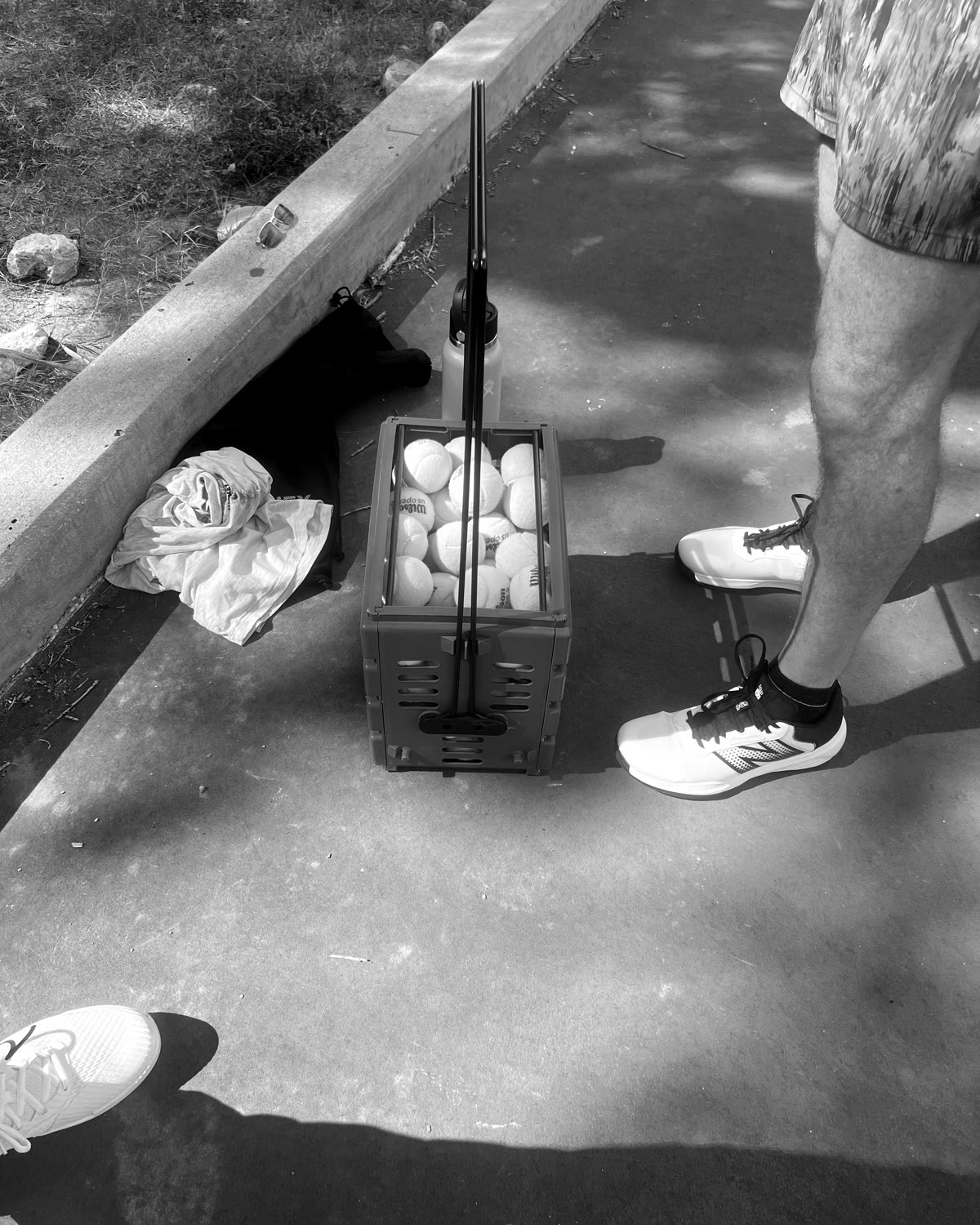 A ball hopper, a towel, and a pair of court shoes