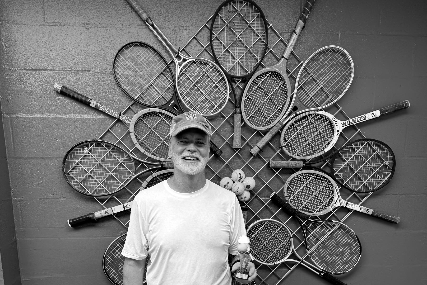 Kevin Edgerton standing in front of a wall of tennis rackets going back decades